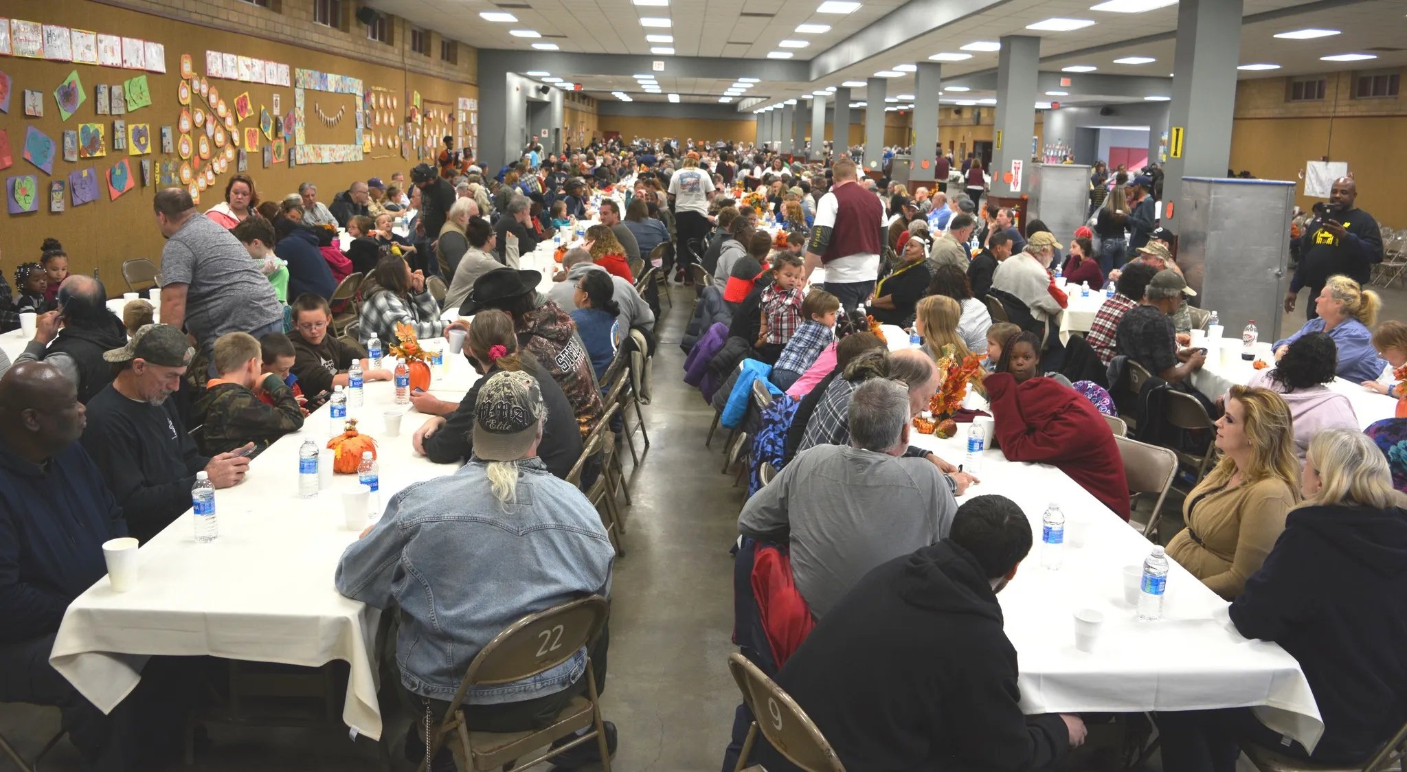 A Community Thanksgiving Dinner fills the hall with neighbors seated together at long tables.